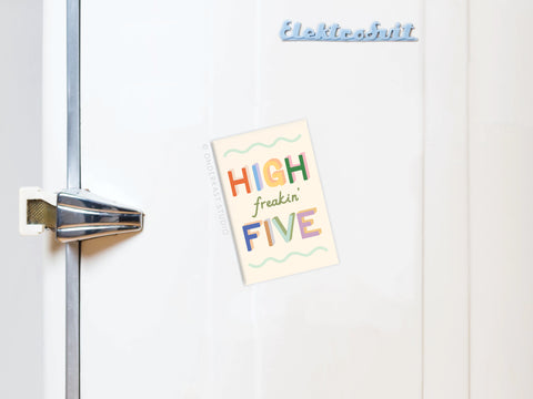 A white fridge with a silver handle displays the High Freakin’ Five Refrigerator Magnet in vibrant colors and playful letters. Onderkast Studio’s brand name is printed in blue script at the top right of the magnet.