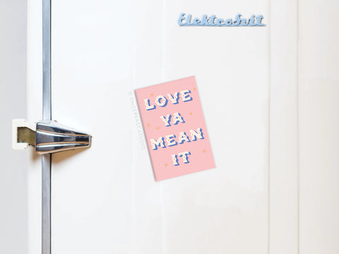 A white fridge with a retro handle displays the Onderkast Studio Love Ya Mean It Refrigerator Magnet, featuring vibrant colors and bold white lettering. ElektroKühl appears in blue at the top.