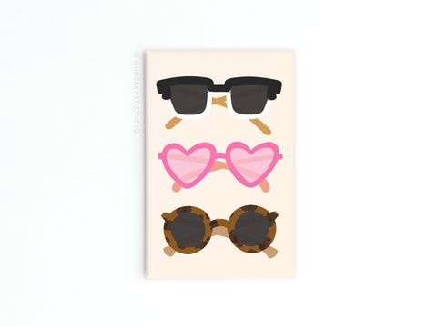 Onderkast Studios Sunglasses Refrigerator Magnet features vibrant prints of three sunglasses—black rectangular, pink heart-shaped, and brown tortoiseshell round—on a light background, perfect for magnetic display.