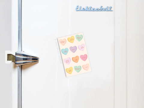 A pastel card featuring the Onderkast Studio Galentine’s Candy Hearts Refrigerator Magnet is attached to a white fridge with a metallic handle, and the “Elektrobit” logo appears on top.