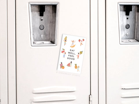 The Onderkast Studio Eat Well Feel Good Refrigerator Magnet features dancing food illustrations and uplifting text, making it a perfect addition to your kitchen decor.