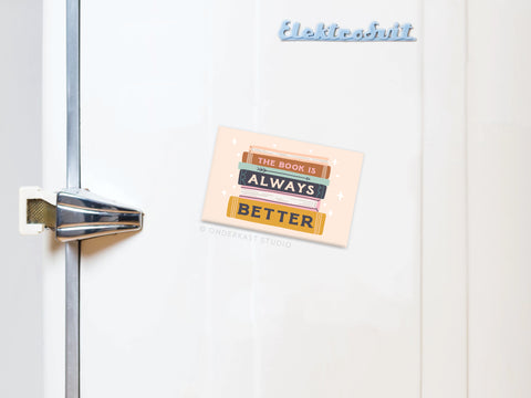 The Book Is Always Better Refrigerator Magnet by Onderkast Studio features the phrase above a stack of colorful books—a perfect find for book lovers.