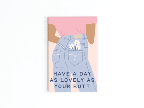 Featuring vibrant colors and an illustration of a person in high-waisted jeans with daisies in the pocket, the Onderkast Studio Lovely As Your Butt Refrigerator Magnet adds fun to your fridge. Text: Have a day as lovely as your butt.