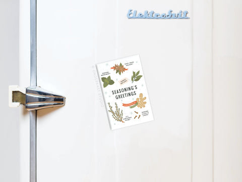 The Seasoning’s Greetings Refrigerator Magnet by Onderkast Studio, featuring charming herbs and spices illustrations, decorates a white fridge for the holidays. The Elektrobit logo is displayed on the fridge’s top right.