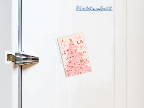 A white fridge with a silver handle displays a pink holiday card and the Fa La La Pink Christmas Tree Refrigerator Magnet by Onderkast Studio, adding festive charm to the décor.