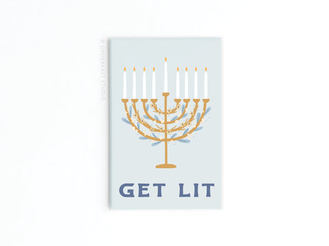 The Get Lit Menorah Refrigerator Magnet from Onderkast Studio features a gold menorah with nine white candles, blue accents, GET LIT in bold blue letters below, and a light gray background—perfect as a festive Hanukkah decoration.