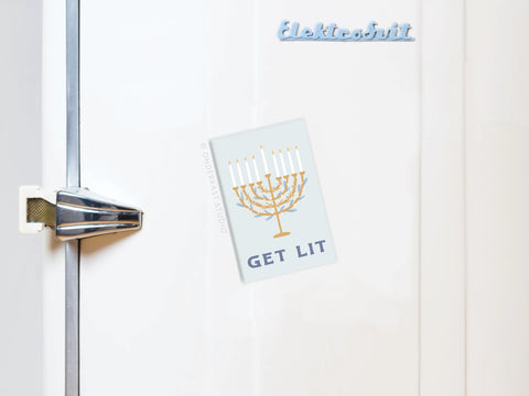 A white fridge with a silver handle features the Onderkast Studio Get Lit Menorah Refrigerator Magnet, displaying a gold menorah with all candles lit—perfect for Hanukkah decor. The blue Elektrobit logo appears on top.