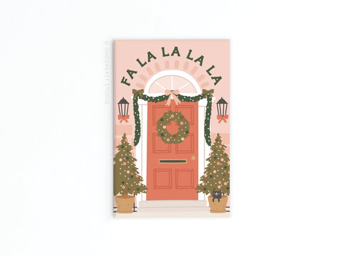 The Fa La La Christmas Door Refrigerator Magnet by Onderkast Studio features a festive door with wreath, garlands, lanterns, potted trees, and FA LA LA LA LA above—perfect for holiday decorating.