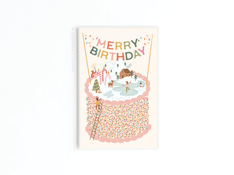 The Merry Birthday Cake Refrigerator Magnet by Onderkast Studio features a festive cake with a snowy winter scene, people, holiday decorations, a ladder leaning on the cake, and a colorful MERRY BIRTHDAY banner above.