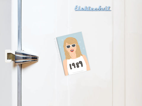 The TS 1989 Refrigerator Magnet by Onderkast Studio features a blonde woman in sunglasses and a 1989 white shirt, adding pop flair to your fridge.