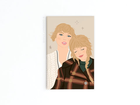 Two illustrated women adorn the Onderkast Studio TS Folkevermore Refrigerator Magnet—one in a white sweater smiles, while the other, with long blonde braids and a plaid jacket, rests her head on her friend’s shoulder, eyes closed.