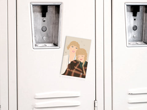 The TS Folkevermore Refrigerator Magnet by Onderkast Studio features a photo of two people—one in plaid, one in a light top—leaning on each other, taped to a white locker with a metal lock, capturing the cozy vibe of Taylor Swift’s evermore.