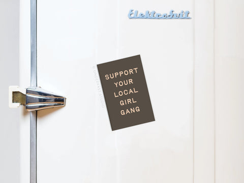 A white fridge with a metallic handle displays the Onderkast Studio “Support Your Local Girl Gang” magnet, celebrating strong women and female solidarity with a stylish touch.