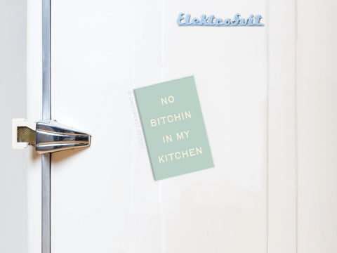 A vintage white USA-made fridge with a silver handle features an Onderkast Studio “No Bitchin’ In My Kitchen” light blue magnet on its door. The word Elektrobit appears at the top.