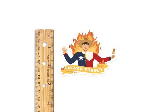 Onderkast Studio’s Never Forget Blazing Big Tex Sticker features weatherproof vinyl with Big Tex in a half-Texas, half-US flag suit, holding a corn dog amid flames and “NEVER FORGET 2012”—a quirky Texas history tribute. Ruler shown for size.