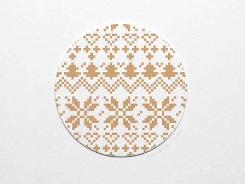 The Holiday Cross Stitch Coaster by Onderkast Studio is a round, white letterpress coaster with a light brown pixel-style geometric pattern—crosses, zigzags, and stars—resting on a plain white surface to showcase its handmade quality.