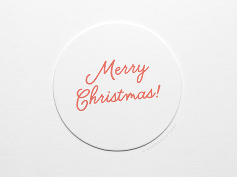 The Merry Christmas Coaster Set by Onderkast Studio features white circular letterpress coasters with Merry Christmas! in red cursive, hand-assembled and gift-ready in a recyclable kraft box.