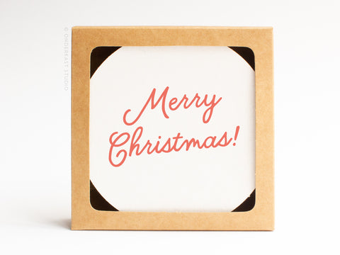 The Merry Christmas Coaster Set by Onderkast Studio comes in a brown, hand-assembled recyclable kraft box with a white card inside that says “Merry Christmas!” in red cursive letters.
