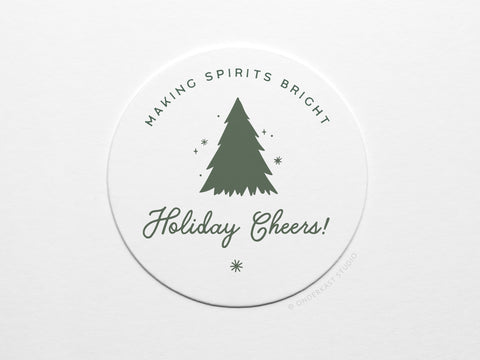 The Holiday Cheers Coaster Set by Onderkast Studio features round white letterpress coasters with a green Christmas tree and stars, “MAKING SPIRITS BRIGHT” above, “Holiday Cheers!” in script below, printed on durable pulp board.