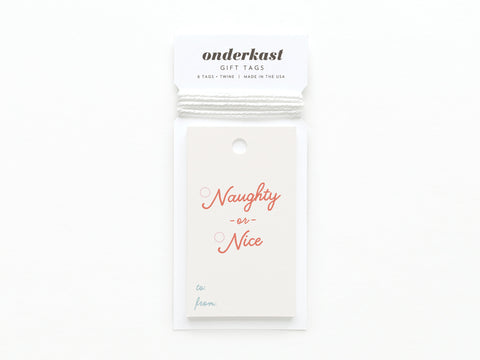 The Naughty or Nice Gift Tag by Onderkast Studio features Naughty or Nice in red script, to: and from: in light blue, is printed in the USA on card stock, attached to white twine, and packaged with an Onderkast GIFT TAGS label.