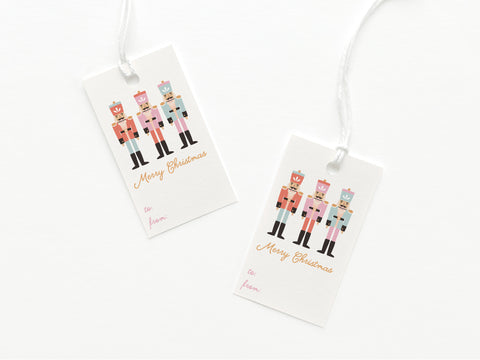 The Merry Christmas Nutcracker Gift Tag by Onderkast Studio is hand-assembled from printed card stock, features three nutcrackers and gold “Merry Christmas” script, includes to/from fields, and is attached with white string.