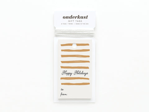 The Onderkast Studio Happy Holidays Swashes Gift Tag features cream and gold stripes, festive text, to/from lines, sturdy card stock, and comes with white twine; proudly printed in the USA.