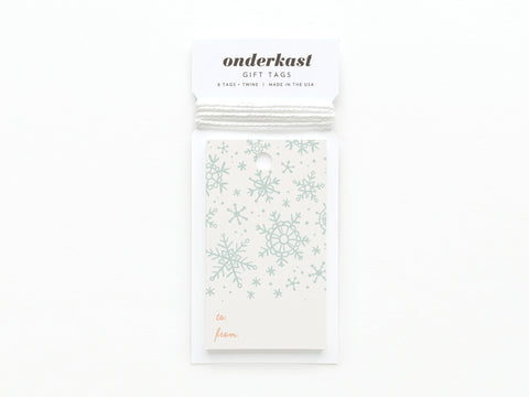 Onderkast Studio’s Snowflakes Gift Tag features vibrant light blue snowflake prints on sturdy card stock, with “to:” and “from:” fields in red and included white string for easy attachment.