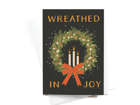 The Wreathed in Joy Folded Greeting Note Set of 10 by Onderkast Studio features a wreath with white berries, green foliage, a red bow, and three lit candles. “WREATHEd IN JOY” is stamped in gold on black. Printed in the USA for a premium feel.
