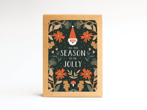 The ’Tis the Season to Be Jolly Folded Greeting Note Set of 10 by Onderkast Studio features festive floral art and a red-hatted elf on a dark background, printed in the USA and framed by orange and yellow flowers.