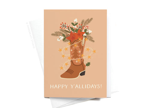 The Happy Y’allidays! Cowboy Boot Folded Greeting Note Set of 10 by Onderkast Studio features a cowboy boot with holiday greenery, red berries, orange flowers, and string lights. “HAPPY Y’ALLIDAYS!” printed at the bottom. Made in the USA.
