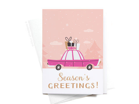 The Seasons Greetings Vintage Car Folded Greeting Note Set of 10 by Onderkast Studio features a pink car with gifts on its roof, gold Seasons Greetings! lettering, and a snowy pink background with trees.