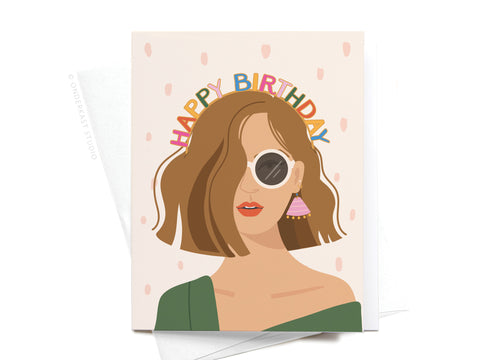 The Happy Birthday Headband - Fair card by Onderkast Studio features an illustrated woman with brown hair, sunglasses, pink earrings, red lipstick, a green top, and arched colorful letters spelling Happy Birthday.