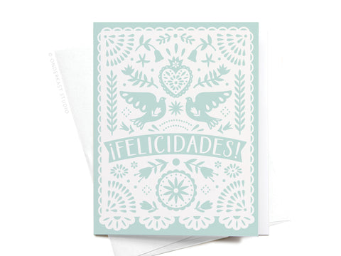 The Felicidades Papel Picado Greeting Card by Onderkast Studio features a white papel picado design with birds, flowers, hearts, and “¡FELICIDADES!” in bold on a light blue background.