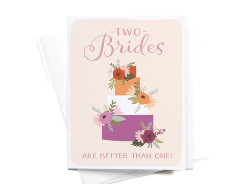 The Two Brides Are Better Than One Greeting Card by Onderkast Studio features a three-tiered wedding cake with floral accents and the phrase Two Brides are better than one! in elegant script, celebrating love and diversity.