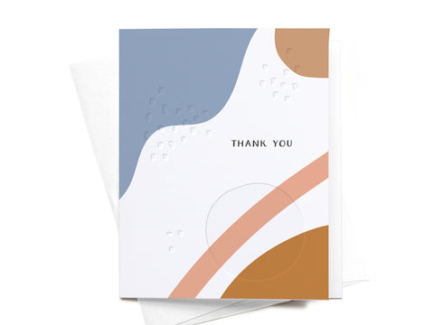 The Onderkast Studio Thank You Abstract Letterpress Greeting Card features blue, white, peach, and mustard shapes with THANK YOU in black at the center. An envelope is partially visible behind the premium-quality card.