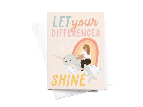 The Onderkast Studio “Let Your Differences Shine Narwhal Sticker Greeting Card” features a girl riding a narwhal on a cloud with a rainbow, plus the text “Let your differences shine,” printed on white card stock.