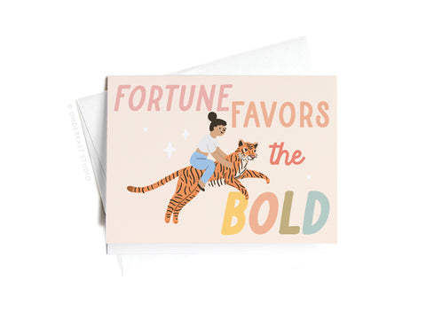 The Fortune Favors the Bold Tiger Sticker Greeting Card by Onderkast Studio features a vibrant illustration of a woman riding a tiger above colorful text on thick white card stock, with a partially visible envelope included.