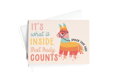 Onderkast Studios Its What Is Inside That Truly Counts Piñata Sticker Greeting Card features a colorful piñata, the phrase “It’s what is inside that truly counts,” and a cheeky speech bubble: “Smack that ass!” Envelope included.