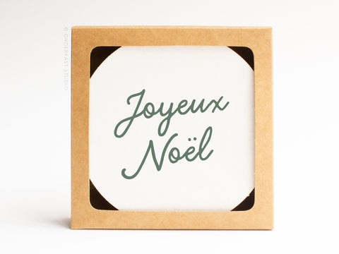 The Joyeux Noël Coaster Set by Onderkast Studio comes in a square brown recyclable box with a white card reading “Joyeux Noël” in green script, making it the perfect gift for letterpress coaster lovers or holiday treasures.