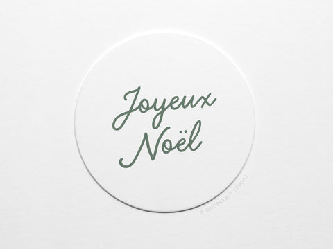The Joyeux Noël Coaster Set by Onderkast Studio features white circular pulp board coasters with Joyeux Noël handwritten in green script, centered on a plain white background.