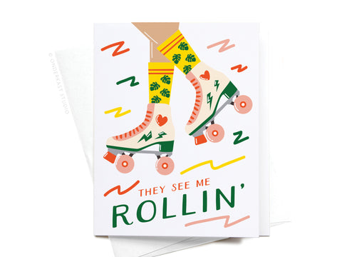 The They See Me Rollin Roller Blades Greeting Card by Onderkast Studio features yellow-socked legs with green leaves and hearts in white and pink skates. “THEY SEE ME ROLLIN” is written below with retro squiggles, perfect for skating fans.