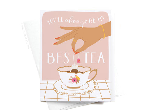 The You’ll Always Be My Bestea Greeting Card by Onderkast Studio features a hand holding a tea bag over a floral teacup on a light background, perfect for tea lovers. Comes with a white envelope.